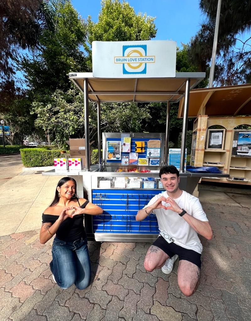 Two students posing in front of the Bruin Love Station metal cart